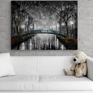 May include: A large canvas print of a nighttime cityscape in shades of gray, black, and orange. The artwork depicts a bridge over a canal, with buildings and trees lining the water's edge. The painting has a textured, impressionistic style.