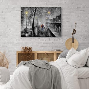 Puede incluir: Impresi&oacute;n art&iacute;stica en lienzo en blanco y negro que representa una escena de calle lluviosa con una pareja caminando bajo farolas. La obra presenta un banco, &aacute;rboles y edificios, con un toque de color en la ropa de la pareja.