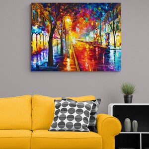 Pode incluir: Uma pintura a &oacute;leo vibrante retrata uma rua da cidade &agrave; noite, refletindo luzes coloridas em uma superf&iacute;cie molhada. A obra apresenta &aacute;rvores, postes de luz e edif&iacute;cios, com uma paleta de vermelhos, amarelos, azuis e roxos. A pintura &eacute; exibida acima de um sof&aacute; amarelo.