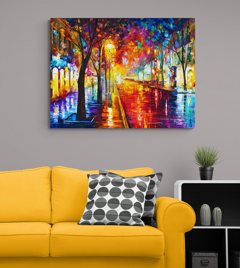 Pode incluir: Uma pintura a &oacute;leo vibrante retrata uma rua da cidade &agrave; noite, refletindo luzes coloridas em uma superf&iacute;cie molhada. A obra apresenta &aacute;rvores, postes de luz e edif&iacute;cios, com uma paleta de vermelhos, amarelos, azuis e roxos. A pintura &eacute; exibida acima de um sof&aacute; amarelo.