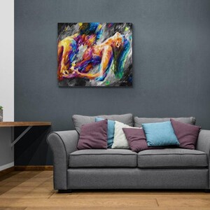 May include: A colorful abstract painting depicting two figures embracing. The artwork features vibrant hues of yellow, blue, and purple against a dark background. The painting is displayed above a gray sofa with decorative pillows.