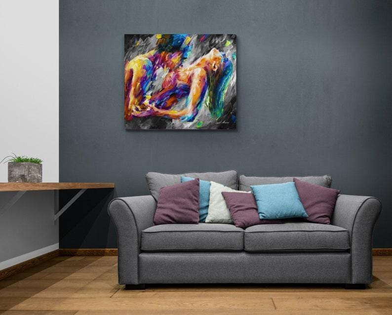 May include: A colorful abstract painting depicting two figures embracing. The artwork features vibrant hues of yellow, blue, and purple against a dark background. The painting is displayed above a gray sofa with decorative pillows.