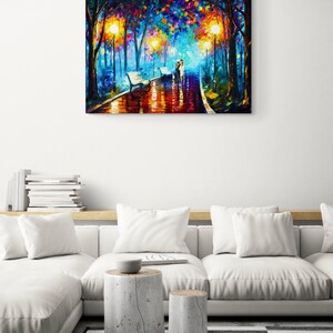May include: A colorful oil painting depicts a park scene with a couple walking on a wet path. The artwork features vibrant hues of blue, orange, and yellow, with streetlights illuminating the path and trees. The painting is displayed above a white sofa.