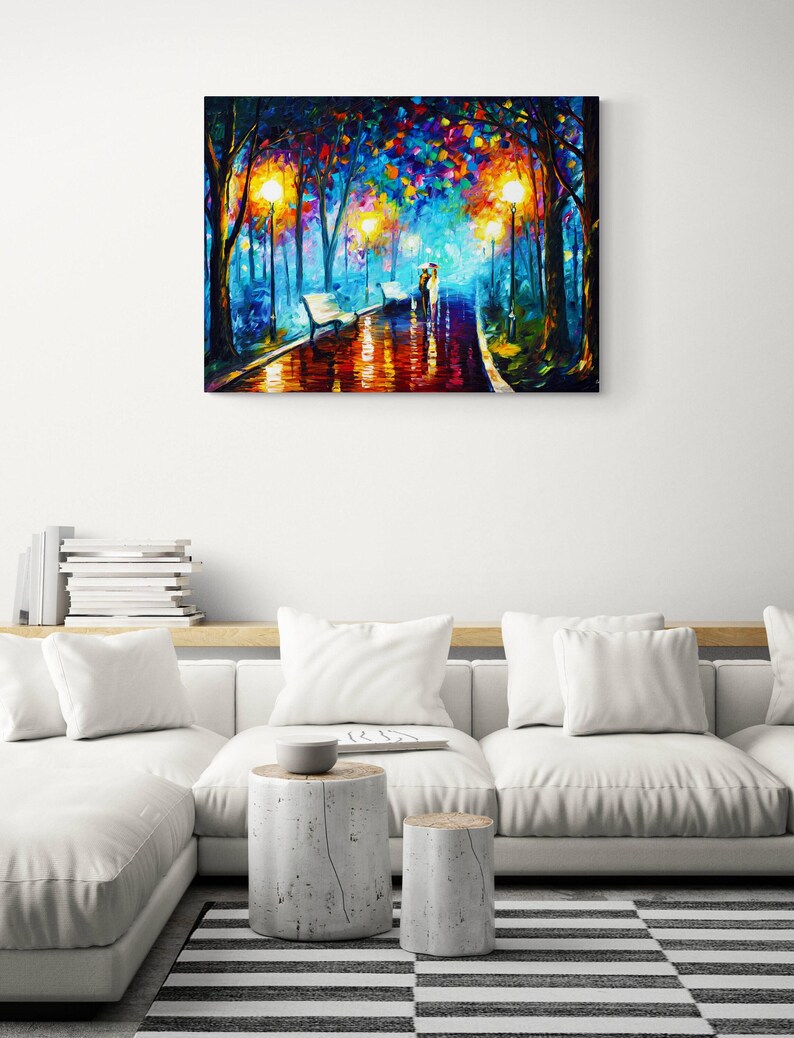 May include: A colorful oil painting depicts a park scene with a couple walking on a wet path. The artwork features vibrant hues of blue, orange, and yellow, with streetlights illuminating the path and trees. The painting is displayed above a white sofa.