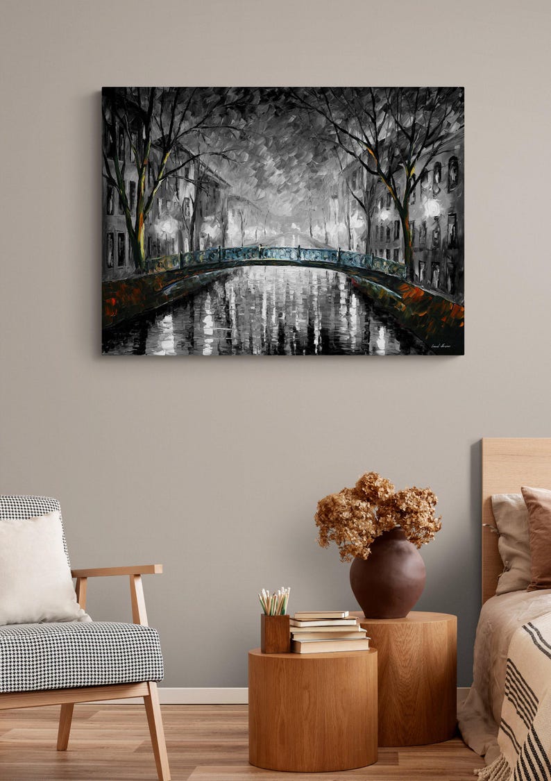 May include: A black and white painting of a canal scene at night. A bridge with blue accents spans the water, reflecting the lights of the buildings and trees along the canal. The artwork is displayed on a wall.