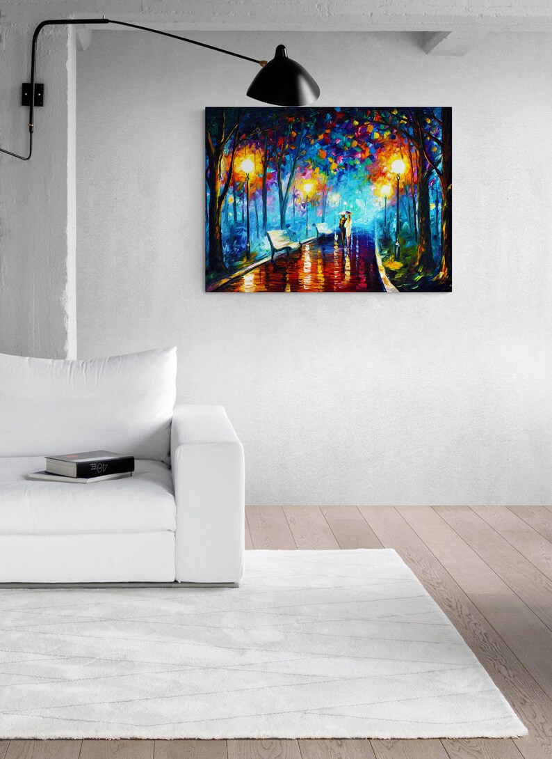 May include: A vibrant oil painting depicts a couple walking on a wet path in a park, illuminated by streetlights. The artwork features a colorful palette of blues, oranges, and yellows, with benches lining the path. The painting is displayed on a white wall above a white sofa.
