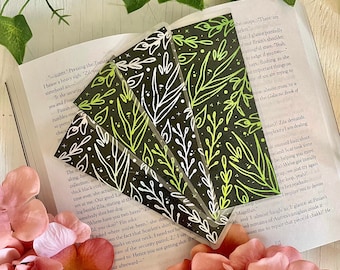 May include: Four black and white bookmarks with a green and white floral design. The bookmarks are layered on top of each other and are surrounded by pink flowers.