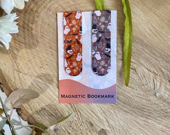 Puede incluir: Dos marcapáginas magnéticos con diseños de Halloween. Uno tiene un fondo naranja con fantasmas y murciélagos. El otro tiene un fondo morado con diseños similares. Las palabras "MAGNETIC BOOKMARK" están impresas en la tarjeta.