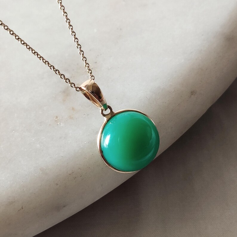 May include: A gold chain necklace with a green gemstone pendant. The pendant is round and has a smooth, polished surface.