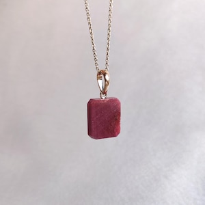 Puede incluir: Un collar de cadena de plata con un colgante cuadrado de color rosa oscuro.