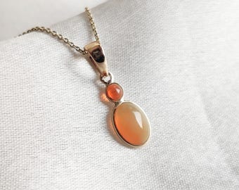Puede incluir: Un collar de cadena de oro con un colgante que presenta dos piedras ovaladas de color naranja.