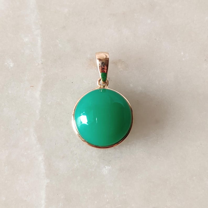 May include: A green gemstone pendant with a gold setting. The pendant is round and has a smooth, polished surface.