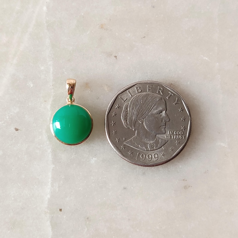 May include: A gold pendant with a round green gemstone. The pendant is about the size of a US dollar coin.