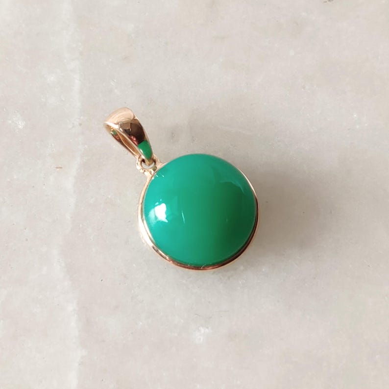 May include: A gold pendant with a round, bright green gemstone.