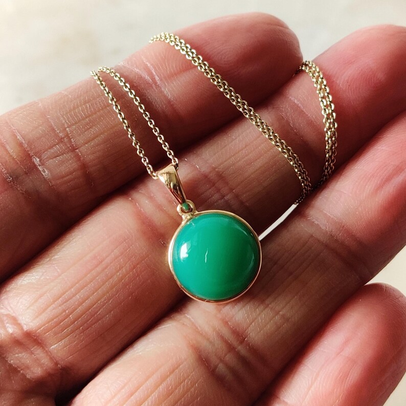 May include: A gold chain necklace with a green gemstone pendant. The pendant is round and has a smooth, polished surface.