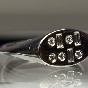 Pu&ograve; includere: Un anello d'argento con una parte superiore ovale incastonata con piccoli diamanti rotondi e rettangolari.