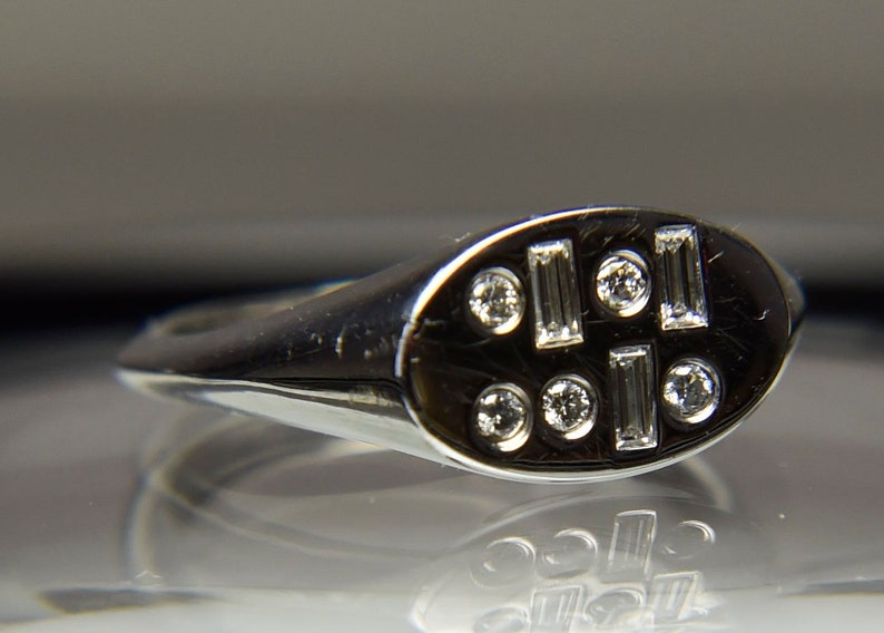 Pu&ograve; includere: Un anello d'argento con una parte superiore ovale incastonata con piccoli diamanti rotondi e rettangolari.