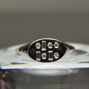 May include: A silver signet ring with an oval top set with small round and baguette-shaped diamonds.
