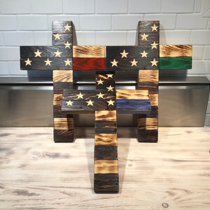 K&ouml;nnte beinhalten: Drei Holzkreuze, jedes mit einem anderen amerikanischen Flaggen-Design. Das obere Kreuz hat ein traditionelles amerikanisches Flaggen-Design, das mittlere Kreuz hat eine d&uuml;nne rote Linie und das untere Kreuz hat eine d&uuml;nne blaue Linie.