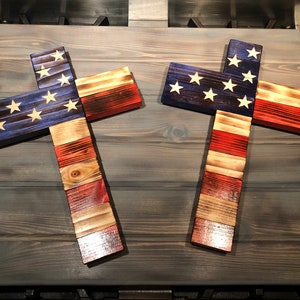 K&ouml;nnte beinhalten: Zwei Holzkreuze, die in den Farben der amerikanischen Flagge bemalt sind. Die Kreuze sind aus wiederverwendetem Holz gefertigt und haben einen rustikalen Look.