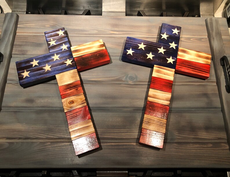 K&ouml;nnte beinhalten: Zwei Holzkreuze, die in den Farben der amerikanischen Flagge bemalt sind. Die Kreuze sind aus wiederverwendetem Holz gefertigt und haben einen rustikalen Look.