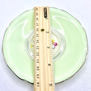 May include: A light green saucer with a silver rim and a floral design in the center. The saucer measures 5 inches in diameter.