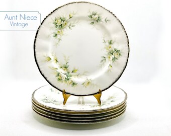 May include: Set of six white ceramic dinner plates with a gold rim and a floral design featuring white roses and green leaves.
