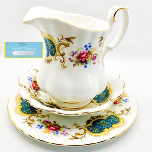 May include: A white porcelain creamer with a gold trim and floral pattern. The creamer has a blue and gold design with a floral motif. It is accompanied by a matching saucer.