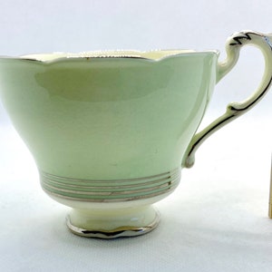 May include: A pale green teacup with a scalloped rim and a silver trim. The cup has a delicate handle and a small base.