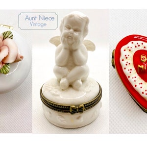 May include: Three vintage porcelain trinket boxes. One is round with a pink rose on the lid. Another is round with a cherub figurine on the lid. The third is heart-shaped with a red heart and the words "Be Mine" in gold lettering.
