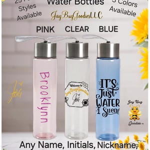 May include: Three 18 ounce reusable water bottles with different designs. The bottles are pink, clear, and blue. The pink bottle has the name "Brooklynn" written on it. The clear bottle has a bee design with the text "Welcome to Jay Bug Goodies". The blue bottle has the text "It's Just Water I Swear" and a bee design. The bottles are available in 25 font styles and 3 colors.