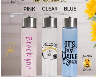 May include: Three 18 oz reusable water bottles with silver lids and carrying straps. The bottles are pink, clear, and blue, featuring custom text including 'BROOKLYNN', 'Welcome to Jay Bug Goodies', and 'IT'S JUST WATER I SWEAR'.