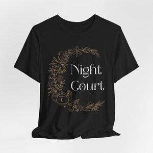 May include: Black t-shirt featuring a gold outline of a crescent moon, flowers, and a teapot with a crescent moon on the lid. The text "Night Court" is in white font.