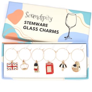 May include: A set of stemware glass charms in a decorative box. Each charm features a gold-colored ring with a different British-themed pendant, including a Union Jack flag, crown, and red telephone booth. The box reads "Serendipity STEMWARE GLASS CHARMS."