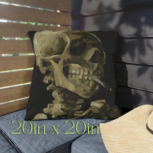 May include: A 20-inch by 20-inch throw pillow with a black background and a painting of a skull smoking a cigarette. The skull is painted in a realistic style with a yellow and brown color palette.