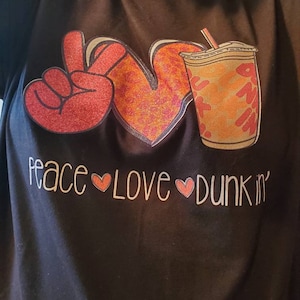 May include: Black t-shirt with a peace sign, heart, and a coffee cup with the text "peace love dunkin'" in white.