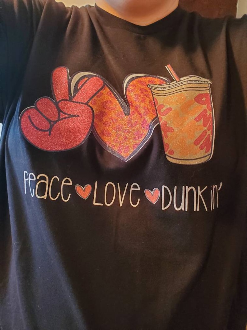 May include: Black t-shirt with a peace sign, heart, and a coffee cup with the text "peace love dunkin'" in white.