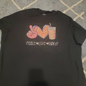 May include: Black t-shirt with a peace sign, heart, and a cup of coffee with the text "Peace Love Dunkin'" printed on it.