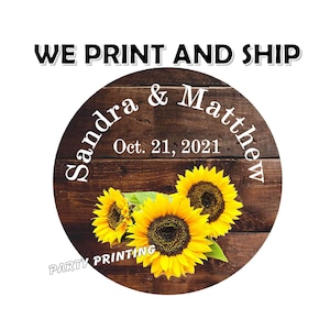 May include: Round wooden sign with a rustic woodgrain background and three yellow sunflowers. The sign says "Sandra & Matthew" and "Oct. 21, 2021" in white text. The text "PARTY PRINTING" is at the bottom of the sign.