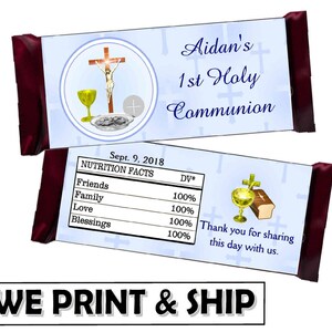 May include: Two chocolate bar wrappers with a religious theme. One features a cross, chalice, and the text "Aidan's 1st Holy Communion." The other displays "Nutrition Facts" and a thank you message. The wrappers have burgundy ends.