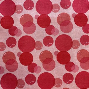May include: Pink fabric with a repeating pattern of red circles of varying sizes. The circles are translucent and overlap each other.