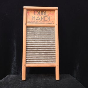 Op de afbeelding: Een vintage houten wasbord met een gegolfd metalen oppervlak. Het wasbord heeft een bord met de tekst "Duble Handi" en "Use either side according to fabric. Columbus Washboard Co. Columbus, O."