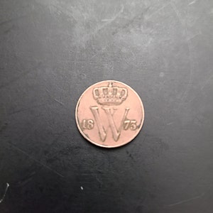 Może przedstawiać: Moneta miedziana z koroną i literą "W" w środku. Rok "1875" jest wygrawerowany wokół krawędzi monety.