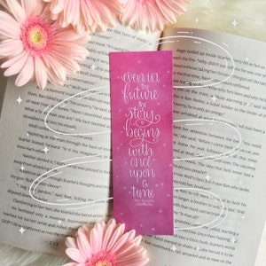 May include: Pink bookmark with a watercolor background and white text that reads "Even in the future the story begins with once upon a time". The bookmark is a great addition to any book lover's collection.
