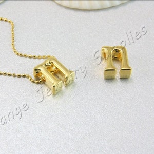 May include: A gold chain necklace with a gold letter 'M' pendant. The pendant is a 3D letter with a square base. The chain is a ball chain.