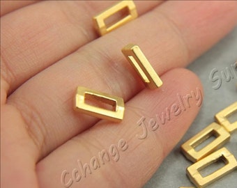 May include: A collection of small, rectangular gold-colored metal jewelry findings. The findings have a hollow, open center and are displayed on a neutral background.