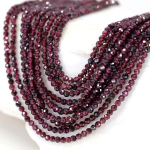 May include: A strand of deep red garnet beads, faceted and strung together. The beads are small and uniform in size, creating a smooth and elegant look.