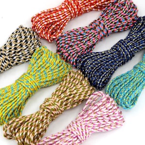 Puede incluir: Una colección de ovillos de cuerda coloridos. La cuerda está disponible en varios colores, incluyendo rojo, negro, dorado, rosa, azul y verde. Cada ovillo está bien enrollado y tiene un brillo metálico, adecuado para manualidades y envolver regalos.