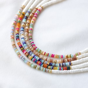 Può includere: Collana multifilo con perline colorate e perline bianche. La collana è realizzata con diversi materiali, tra cui pietre naturali e conchiglie.