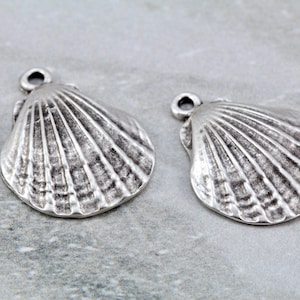 Peut inclure: Deux breloques en forme de coquillage en métal argenté avec une boucle en haut pour les attacher à des bijoux ou des objets artisanaux.